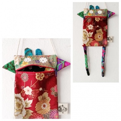 Bolsa pendente de tecido floral colorido com orelhas e pernas, pendurada numa parede branca.