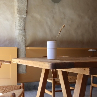 Mesa de madeira com copo branco e cadeira trançada em ambiente com parede bege