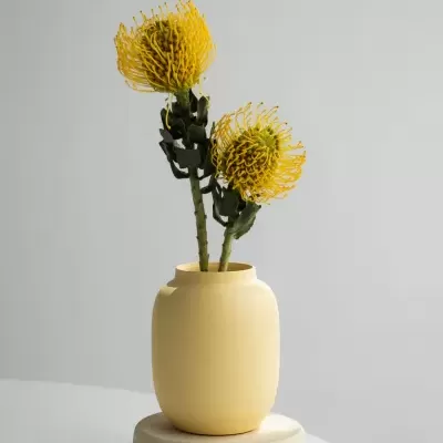 Vaso amarelo com flores artificiais amarelas sobre suporte redondo