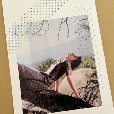 Fotografia de mulher de vestido xadrez sobre uma rocha com bordados em pontos coloridos na moldura branca.