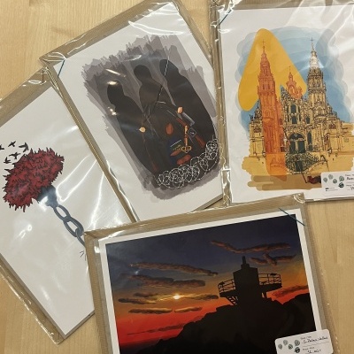 Quatro postais ilustrados em embalagens transparentes em cima de mesa de madeira clara.