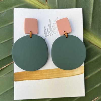 Brincos redondos verdes e retangulares cor de rosa sobre cartão branco com linha dourada e folha desenhada