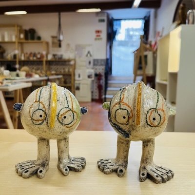 Dois bonecos de cerâmica com pés grandes em mesa num interior de loja
