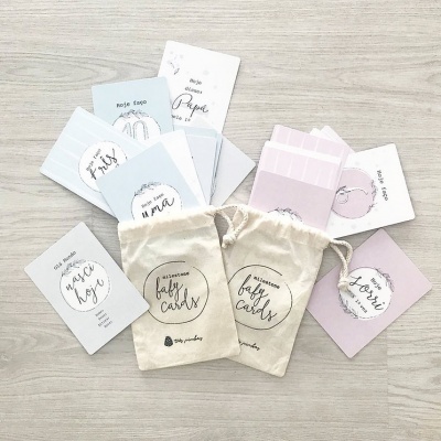 Cartões de bebé coloridos com texto manuscrito e sacos de algodão cru em fundo de madeira clara