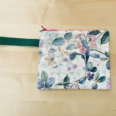 Bolsa pequena floral com fecho cor-de-rosa e alça verde sobre madeira clara