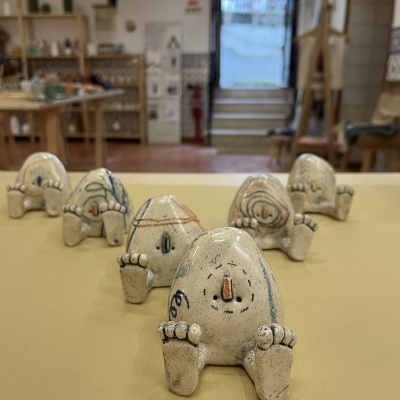 Seis esculturas de cerâmica com desenhos coloridos sobre superfície amarela em ambiente interior.