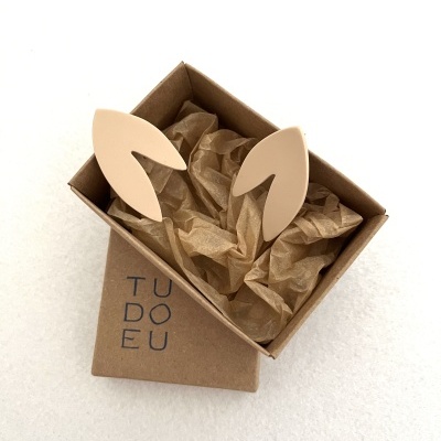 Brincos beje forma de folhas em caixa de cartão marrom com papel de seda castanho claro e texto TUDO DEU na tampa