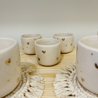 Conjunto de copos em cerâmica branca com corações dourados em superfície de madeira com suportes trançados