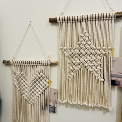 Dois painéis de parede macramé creme com padrões de coração e estrela pendurados