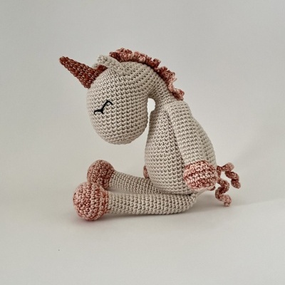 Boneco de unicórnio de croché creme com detalhes rosa sentado
