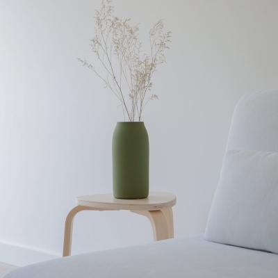 Vaso verde fosco com ramos secos em banco de madeira ao lado de sofá branco