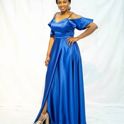 Mulher com vestido azul longo acetinado e sapatos de salto alto nude.