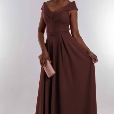 Mulher com vestido comprido castanho escuro e carteira cor de rosa bege