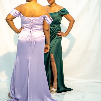 Duas mulheres com vestidos cetim lilás e verde-escuro, em fundo branco.