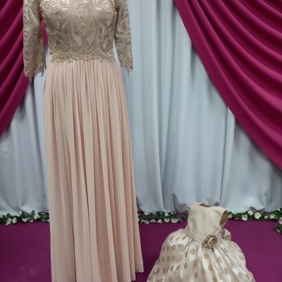 Vestidos bege feminino e infantil com detalhes dourados e fundo de cortinas vinho e branco