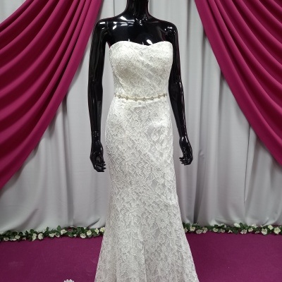 Vestido de noiva branco de renda em manequim preto com cortinas rosa e branca ao fundo