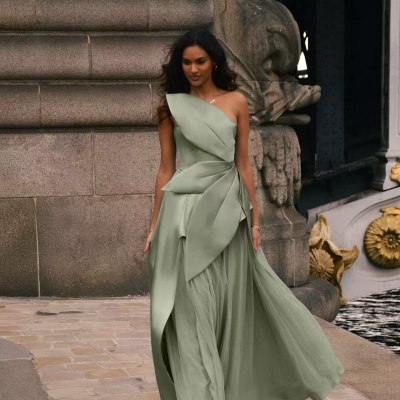 Mulher com vestido longo verde-clarinho fluido, parede de pedra e ornamentos dourados ao fundo
