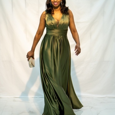 Mulher com vestido longo verde acetinado e mala dourada em fundo branco