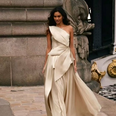Vestido longo creme com ombro único e detalhes drapeados num cenário exterior