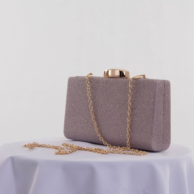 Bolsa clutch cinza com corrente dourada e fecho metálico sobre superfície branca.