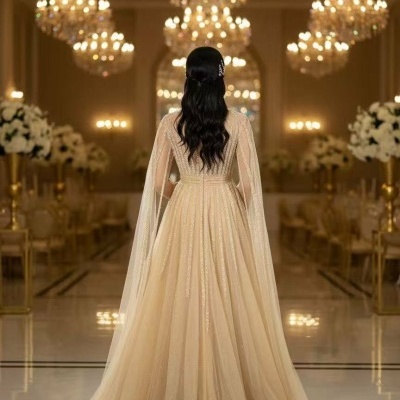 Vestido longo bege dourado com brilho e mangas transparentes em ambiente luxuoso com lustres e flores