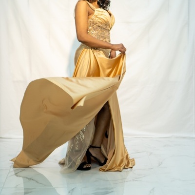 Vestido dourado longo de cetim bordado com transparência e sapatos pretos em fundo branco