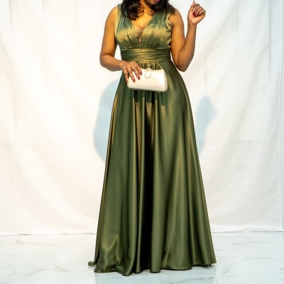 Mulher com vestido longo verde cetim e carteira bege sobre chão de mármore.