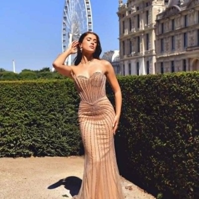 Vestido de festa bege comprido com brilho e detalhes verticais, usado por mulher em parque