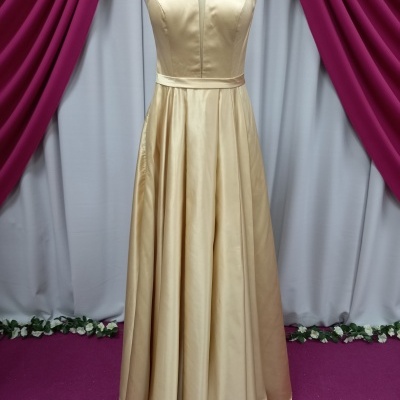 Vestido longo dourado acetinado em manequim com fundo de cortinas vinho e lilás