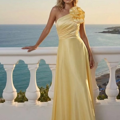 Vestido longo amarelo com alça única e flor no ombro à beira-mar