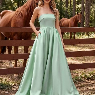 Vestido longo sem alças verde pastel com saia rodada e bolsos, com mulher ao ar livre junto a cerca com cavalos