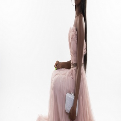 Mulher sentada de perfil com vestido longo rosa e carteira prateada