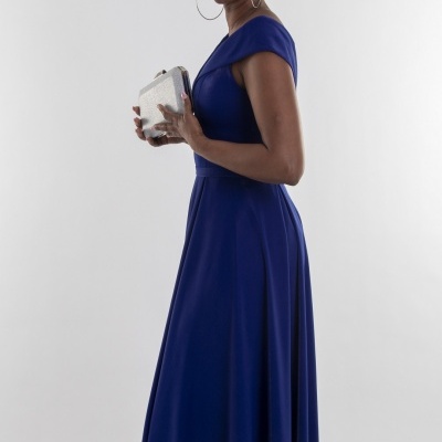 Mulher com vestido longo azul escuro e carteira prateada num fundo branco