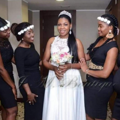 Noiva com vestido branco e bouquet cercada por cinco mulheres em vestidos pretos e coroas de flores brancas