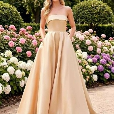 Vestido de festa comprido bege claro com saia larga e bolsos, ao ar livre com flores ao fundo