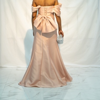 Mulher de vestido longo rosa com laço grande nas costas e bolsa prateada