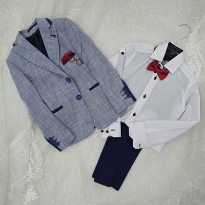 Conjunto infantil com blazer xadrez, camisa branca, gravata borboleta vermelha e calças azul escuro sobre tecido branco brilhante