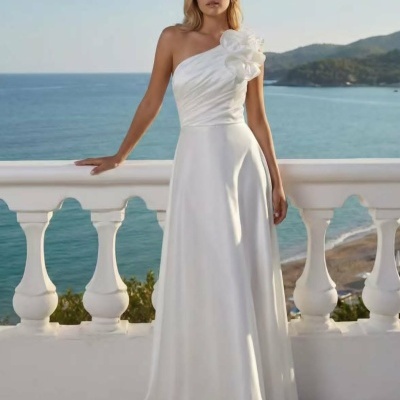 Vestido longo branco com um ombro só e flor no ombro, ao ar livre numa varanda com vista para o mar.