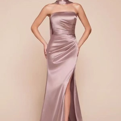 Vestido longo de cetim rosa chá com racha alta, usado por mulher com cabelo preso e fundo bege.