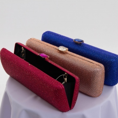 Três carteiras de mão brilhantes nas cores vermelha, dourada e azul sobre mesa com toalha branca