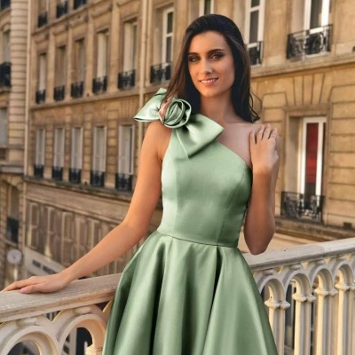 Vestido verde de cetim com laço no ombro e cenário urbano ao fundo