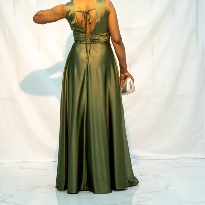 Vestido longo verde-oliva acetinado com costas abertas, carteira prata, mulher vista de costas em fundo branco