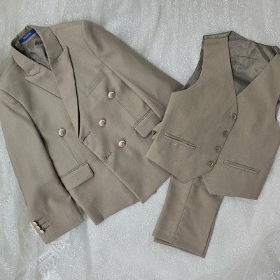 Conjunto bege de casaco, colete e calças em tecido liso sobre fundo branco brilhante e renda.