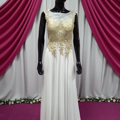 Vestido longo branco com renda dourada em manequim negro diante de cortinas rosa e branca