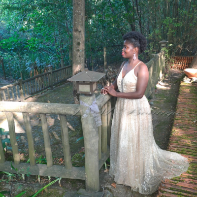 Mulher com vestido branco rendado em ambiente exterior junto a corrimão e poste de madeira