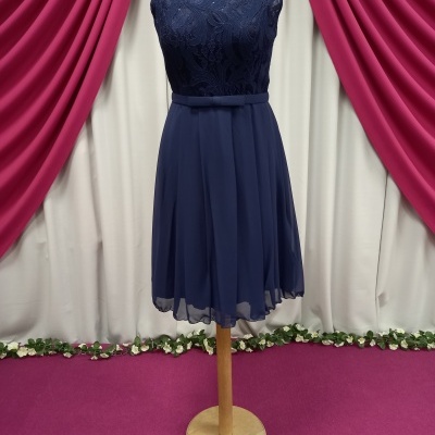 Vestido azul escuro em renda e tecido fluído num manequim com fundo de cortinas cor de rosa.