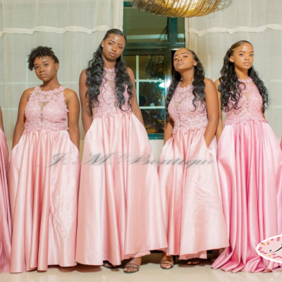 Seis mulheres em vestidos rosas longos com detalhes em renda, em ambiente interno com cortinas brancas