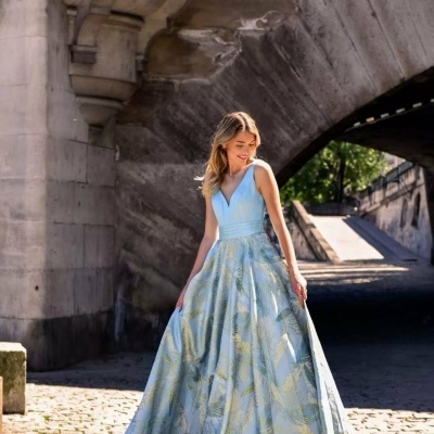 Vestido longo azul claro com padrão dourado de folhas junto a arcada de pedra