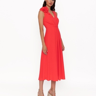 Vestido midi vermelho com flor no ombro e sandálias douradas.