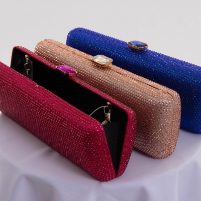 Três malas clutch brilhantes em vermelho, dourado e azul sobre tecido branco